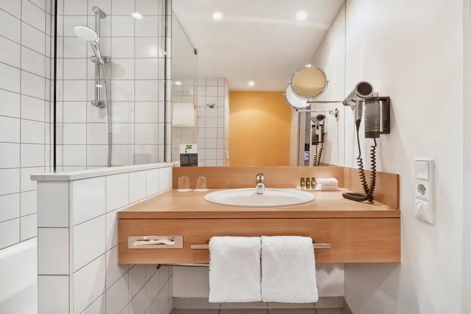 Badezimmer mit einem Waschbecken und einer Dusche daneben. Über dem Waschbecken hängt ein großer Spiegel.