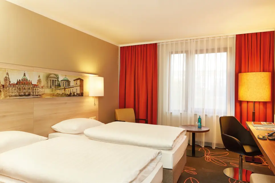 Zwei getrennte Betten vor einem Schreibtisch. Neben dem einen Bett steht ein Stuhl und ein Tisch.