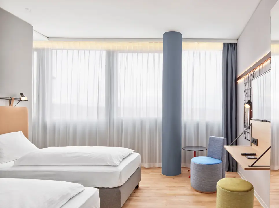 Twinbetten vor Fenstern. Vor dem Bett stehen Hocker und ein Schreibtisch.